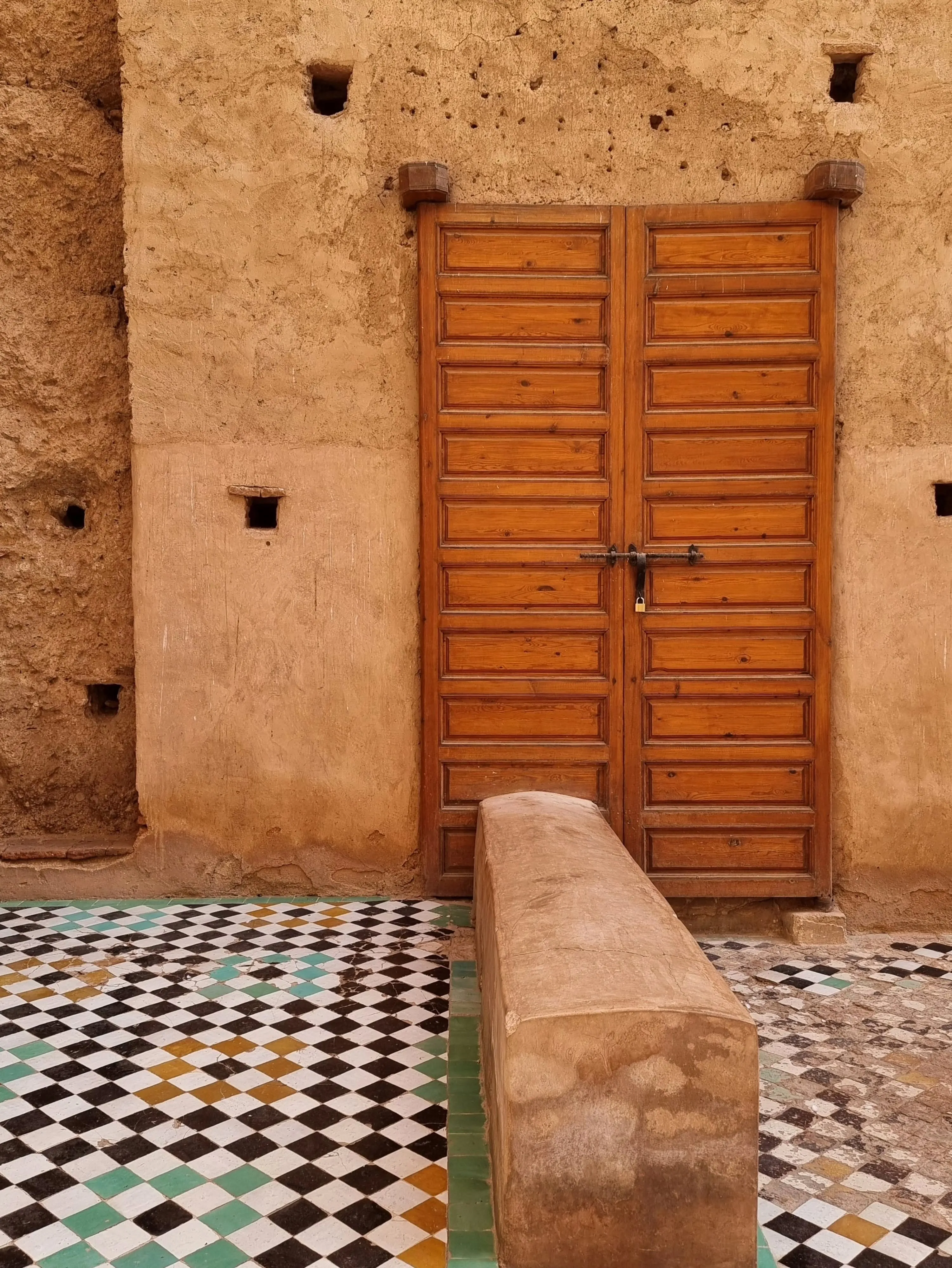 An ochre wall with a carved wooden door and a checkerboard tiled floor in Andalusia.