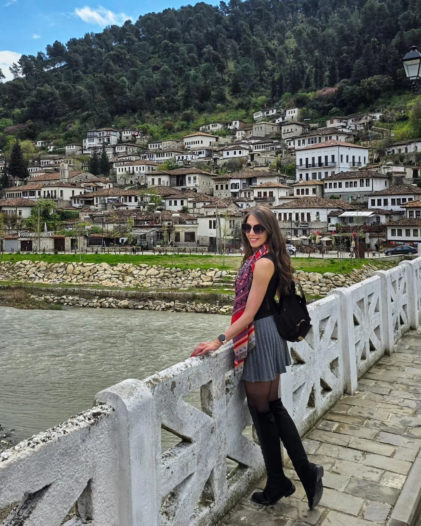 Deena on a bridge in Berat, Albania, the tiered Ottoman houses on the hill behind.