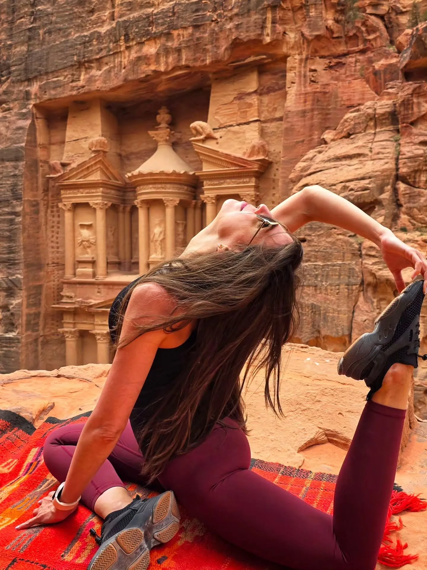 Deena in a deep backbend on a kilim, the sandstone of Petra behind her.