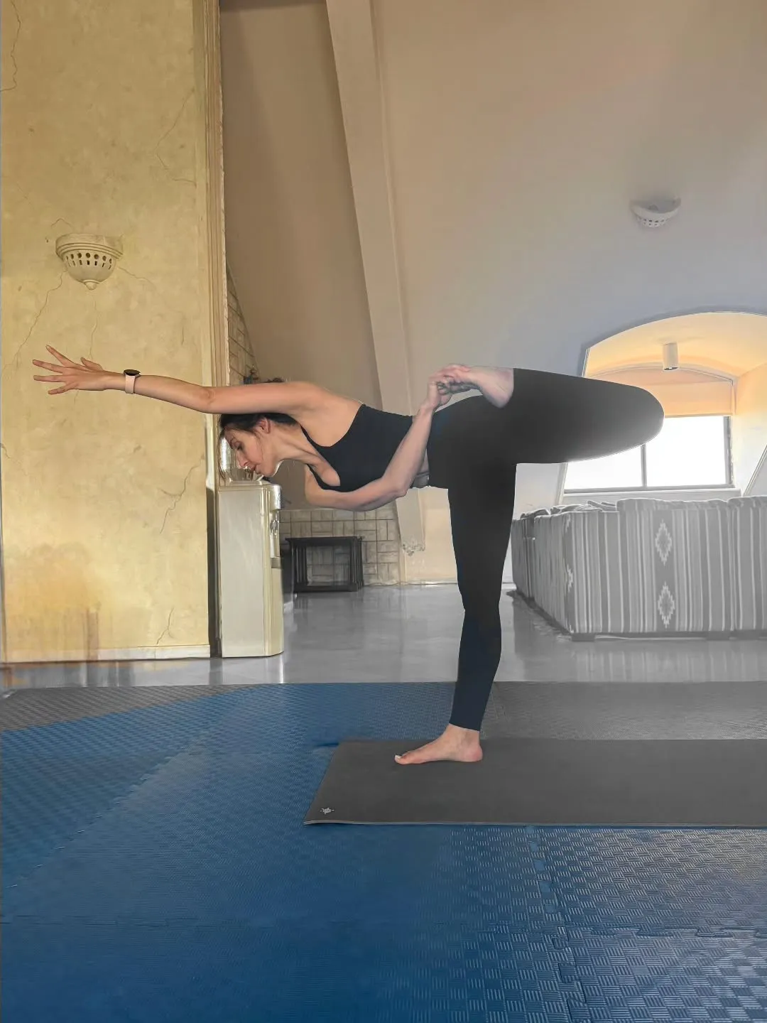 Deena balancing on one leg in a warm studio room.