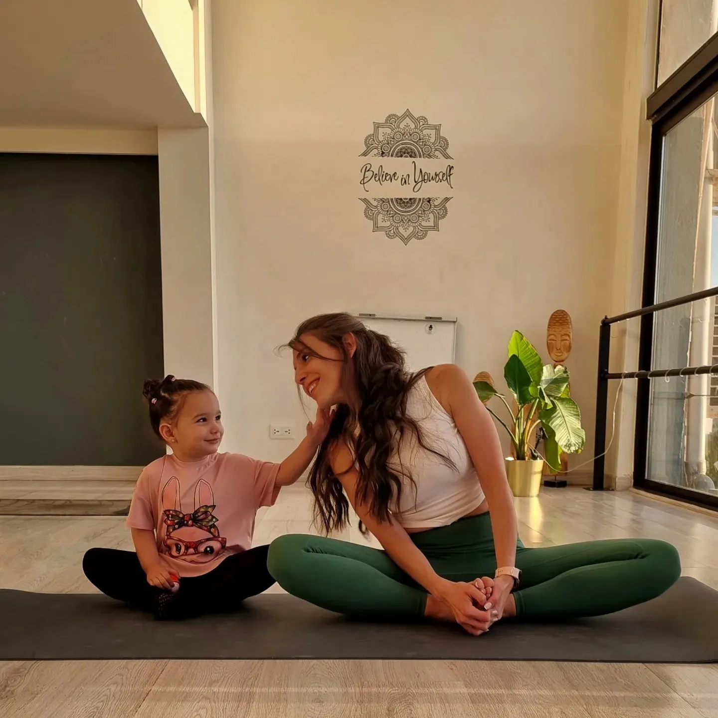 Deena sitting on a mat with a young child, both laughing.